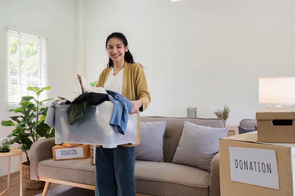 Asian woman holding box full of second hand clothes to donate. Help poor people